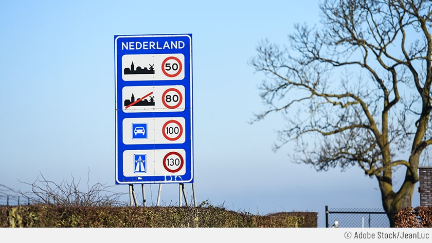 Zu sehen ist ein blaues Verkehrsschild zu sehen, auf dem in weißer Schrift „NEDERLAND“ steht. Unter dem Schriftzug sind die verschiedenen Geschwindigkeitsbegrenzungen in den Niederlanden abgebildet.