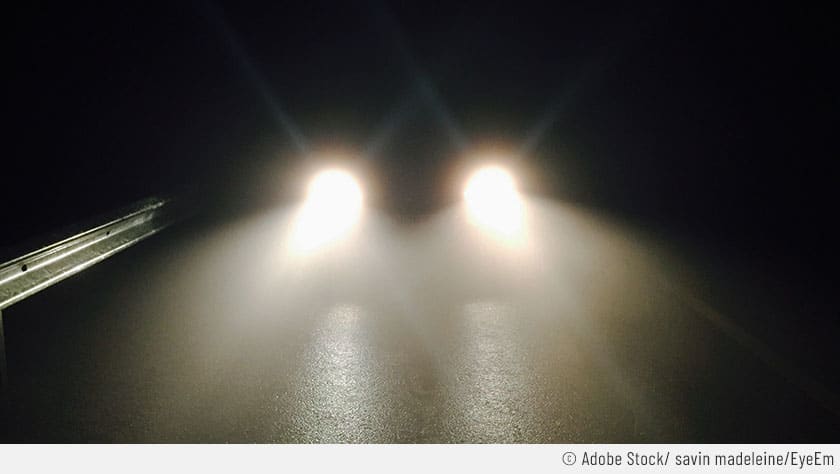 Auf dem Bild ist ein Fahrzeug mit eingeschaltetem Fernlicht zu sehen. Das Auto fährt nachts auf einer Landstraße.
