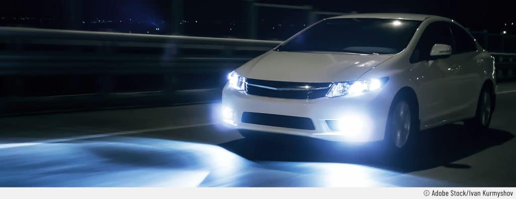 Auf dem Bild ist ein weißes Auto mit eingeschaltetem Fernlicht zu sehen. Man sieht auch den Lichtkegel der LED-Scheinwerfer.