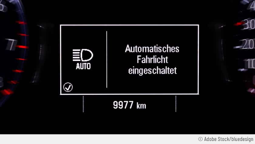 Im Cockpit eines Autos wird das Symbol für den Fernlichtassistenten angezeigt. Dort ist auch die Meldung zu sehen "Automatisches Fahrlicht eingeschaltet".