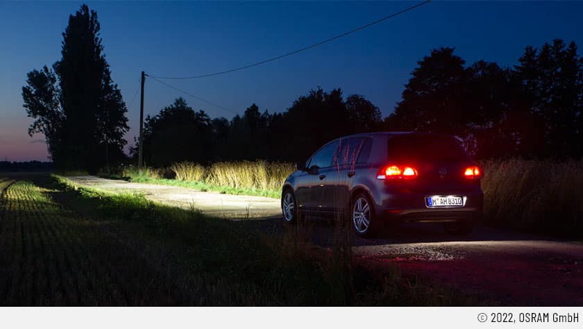 Das Fahrzeug auf dem Bild steht auf einer verlassenen Landstraße, die links und rechts von beackerten Feldern umgeben ist. es ist dunkel und die Bremslichter sind an; die Frontscheinwerfer leuchten dank Retrofit-LEDs bestens.