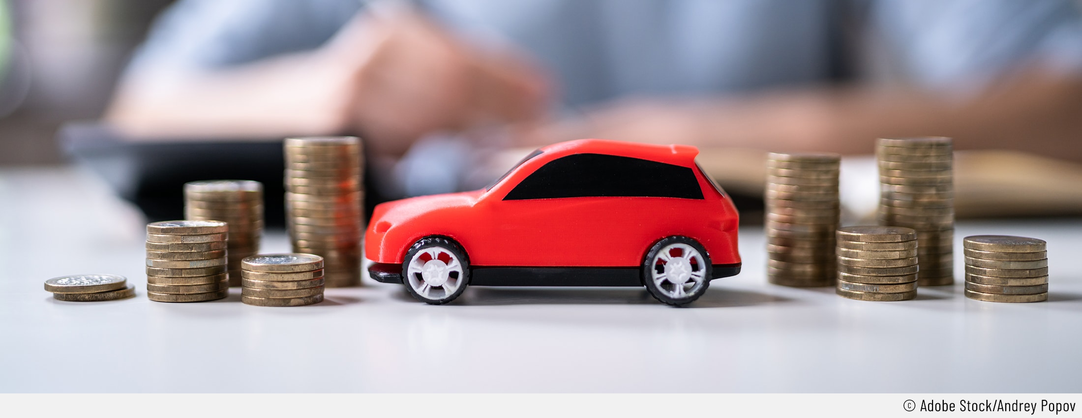Auf dem Bild sind mehrere Münzstapel neben einem roten Spielzeugauto zu sehen. Das soll die Unterhaltskosten eines Autos verbildlichen.