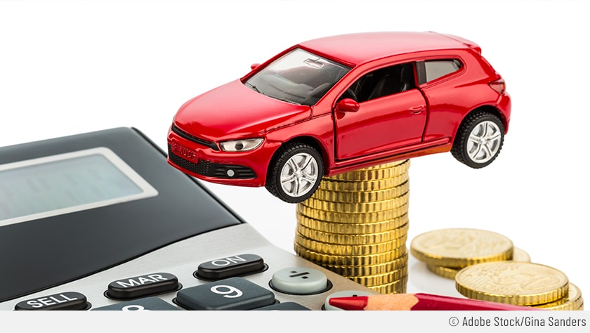 Auf dem Bild ist ein rotes Spielzeugauto auf einem Münzstapel zusehen. Daneben ist ein Taschenrechner.