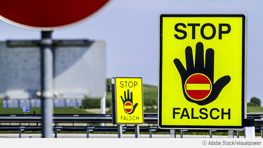 Auf dem Bild sieht man ein Geisterfahrer-Verkehrszeichen, das nochmal verdeutlicht, dass es dortlang in die falsche Richtung geht. Auf dem grellgelben Schild steht "STOP FALSCH" mit einer ausgestreckten Hand und einem "Durchfahrt-verboten"-Zeichen.