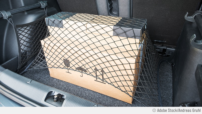 Auf dem Bild sieht man ein Paket im Kofferraum, das mit einem Gepäcknetz gegen Verrutschen gesichert ist.