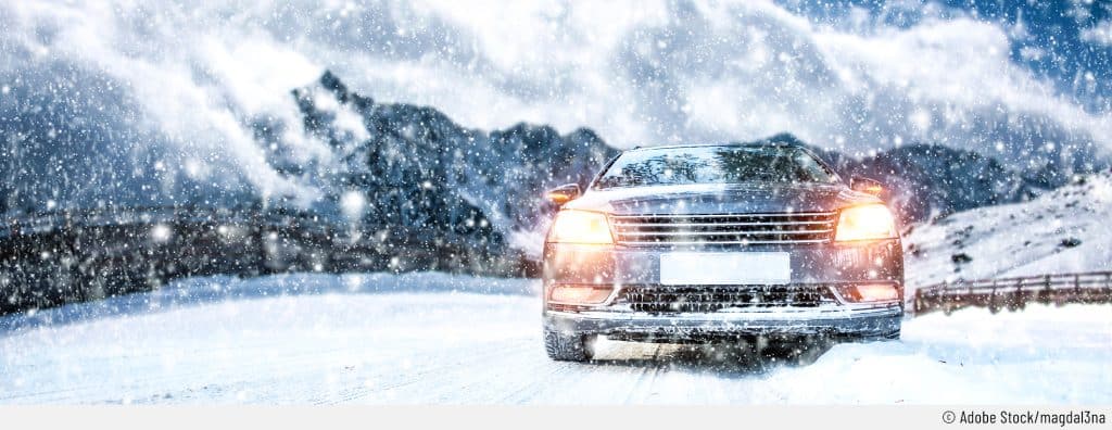 Auf dem Bild ist ein Auto von vorne zu sehen, das auf einer schneebedeckten Straße fährt. Es ist nicht nur glatt, die Sicht ist auch noch durch starken Schneefall eingeschränkt.
