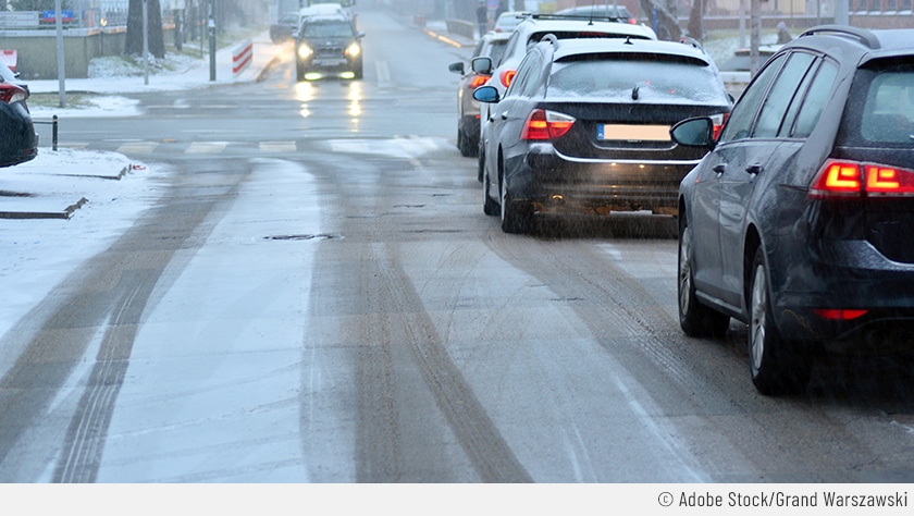 Auf dem Bild sind Autos zu sehen, die an einer roten Ampel halten. Hier liegt allerdings Schnee auf der Straße, sodass die Rutschgefahr beim Bremsen erhöht ist.
