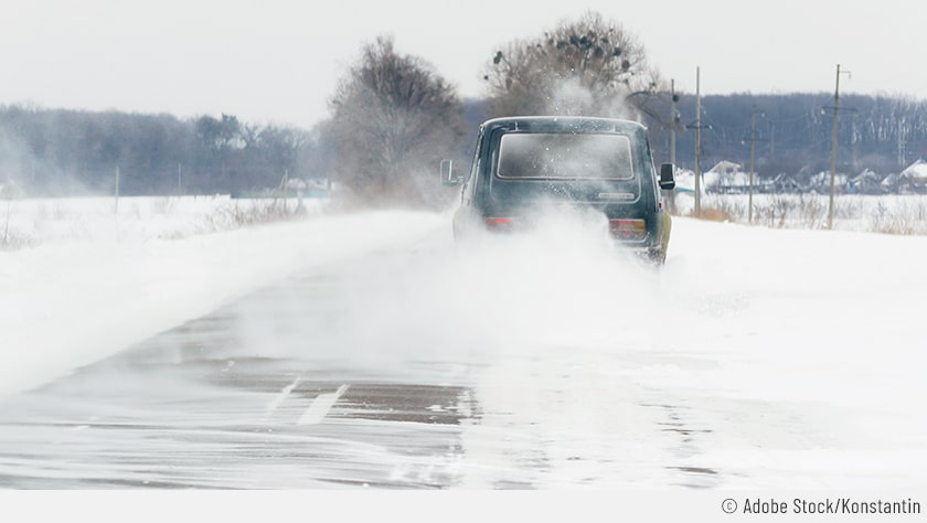 Auf dem Bild ist ein Auto zu sehen, das auf einer schneebedeckten Straße fährt. Durch den aufgewirbelten Schnee ist die Sicht des Hintermanness startk eingeschränkt. Daher sollte beim Fahren im Schnee ein größerer Sicherheitsabstand eingehalten werden.