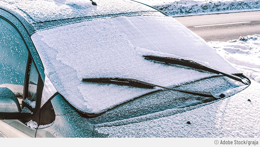 Auf dem Bild sieht man ein Auto, das eingefroren ist. Auf der Windschutzscheibe ist eine Frostschutzdecke angebracht, um das Eiskratzen zu vermeiden.