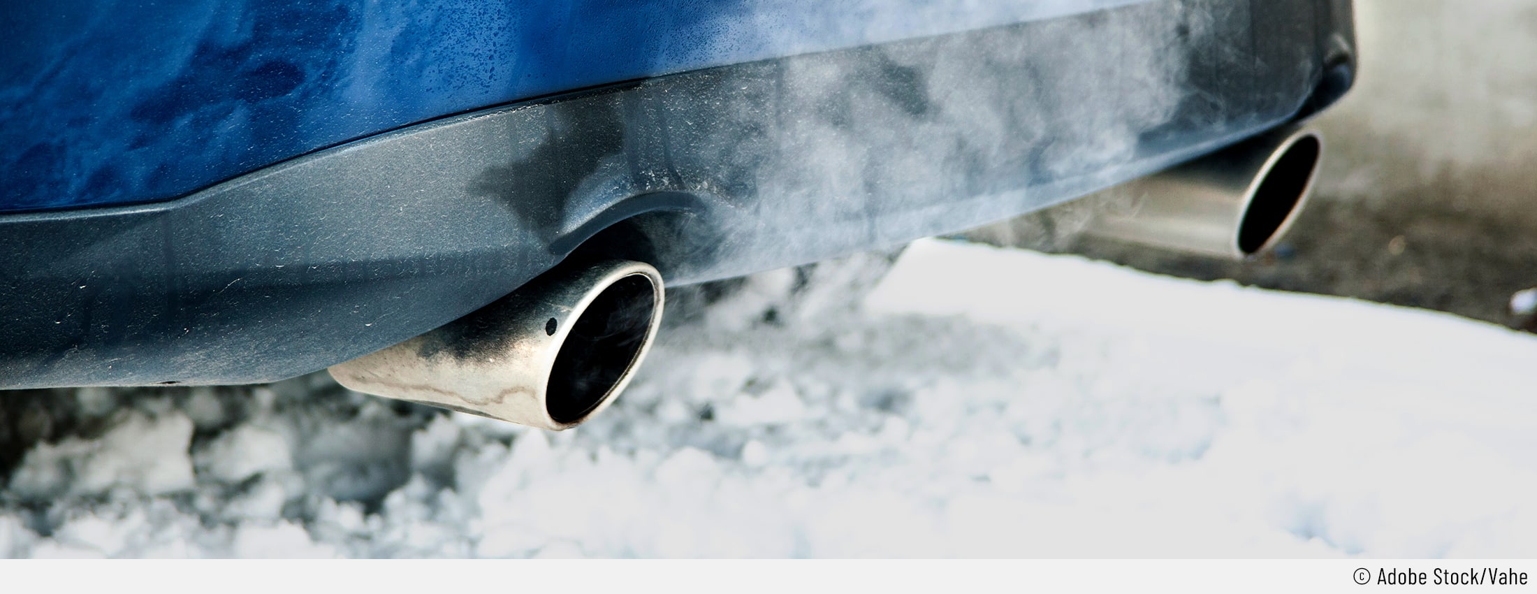 Auf dem Bild ist zu sehen, dass ein Auto auf Schnee steht. Der Fokus ist auf dem Auspuff, aus welchem Rauch kommt, weil jemand das Auto warmlaufen lässt.