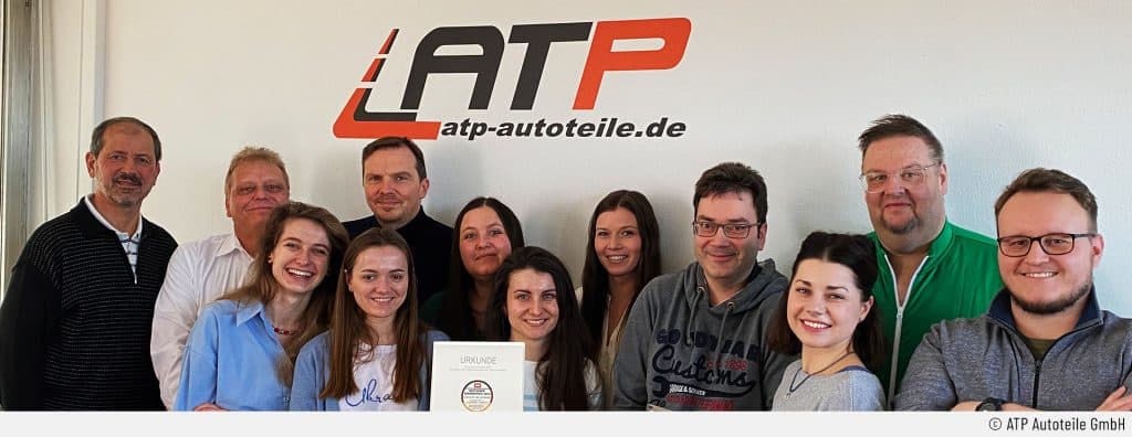 Der Erhalt des Deutschen Servicepreises 2023 will gebührend gefeiert werden: Der Kundensupport und der Geschäftsführer Alexander Bugge von ATP Autoteile sind stolz auf die erhaltene Urkunde und lächeln in die Kamera.