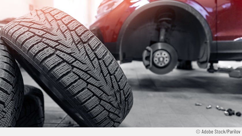 Auf dem Bild sieht man ein aufgebocktes rotes Auto beim Reifenwechsel. Der Fokus liegt dabei auf den abmontierten Reifen im Vordergrund.