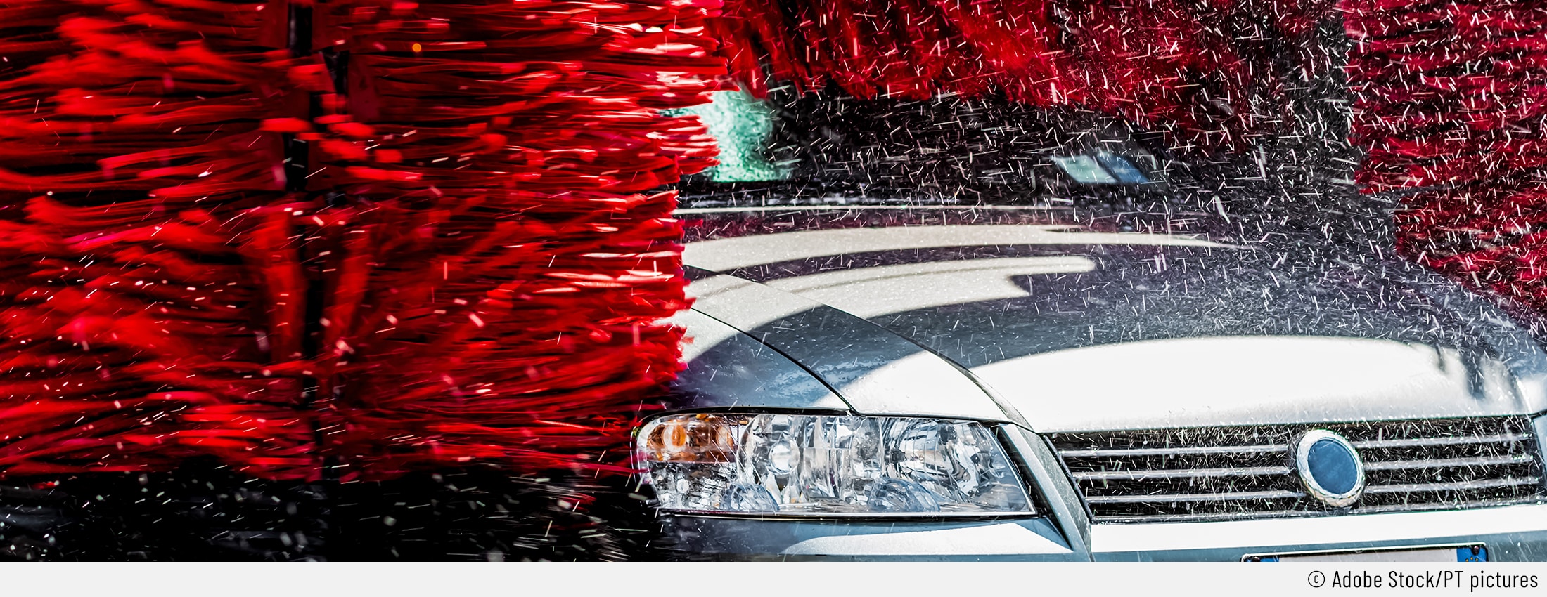 Auf dem Bild ist ein silbernes Auto von vorne zu sehen, das gerade durch eine automatische Waschanlage fährt. Die roten Waschbürsten der Waschanlage können Kratzer verursachen.