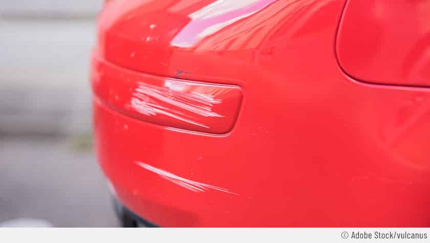 Auf dem Bild sieht man als Nahaufnahme das Heck eines roten Autos. Der Fokus liegt auf mehreren Lackkratzern durch eine Waschanlage.
