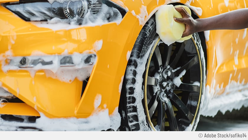 Auf dem Bild ist zu sehen, wie jemand ein gelbes Auto selbst wäscht, um Waschanlagen-Kratzer zu vermeiden.
