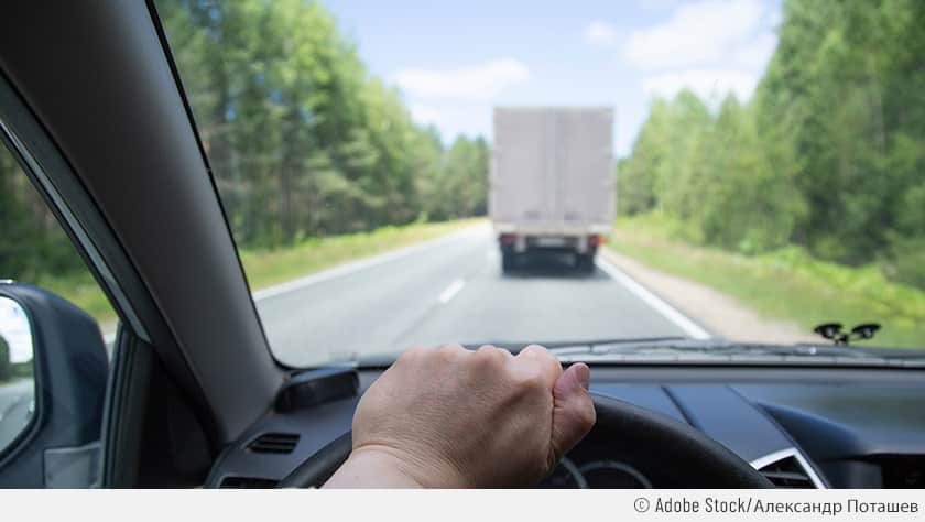 Aus Fahrerperspektive sieht man die linke Hand am Lenkrad und einen vor dem Auto fahrenden Lkw. Die Autofahrer ist kurz davor, den Überholvorgang zu starten.