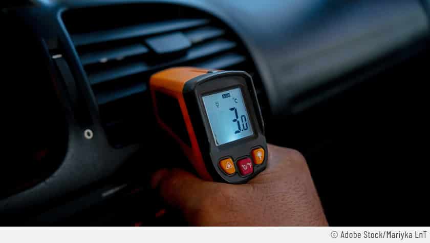 Auf dem Bild ist zu sehen, wie eine Person anhand eines Infrarot-Thermometers die Temperatur der Klimaanlage im Auto selber zu prüfen versucht.