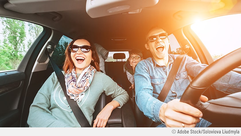 Zu sehen ist eine Familie mit glücklichen Gesichtausdrücken bei einer langer Autofahrt.