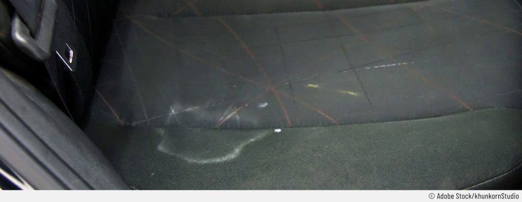 Ein unschöner Salzwasserfleck mit weißem Rand ist auf einem dunklen Autositz.