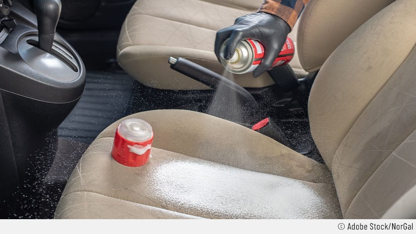 Eine Person sprüht die Autositze mit einem Reinigungsschaum ein, um die Autositze zu reinigen. Um Hautreizungen zu vermeiden, trägt die Person Einweg-Gummihandschuhe bei der Sitzpolster-Reinigung.