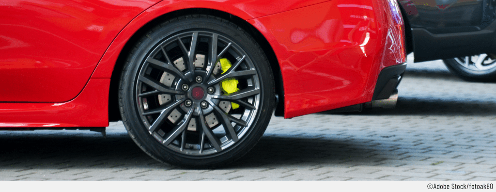 Auf dem Bild ist das hintere Rad eines roten Autos zu sehen. durch Felge erkennt man einen Bremssattel, der gelb lackiert wurde.