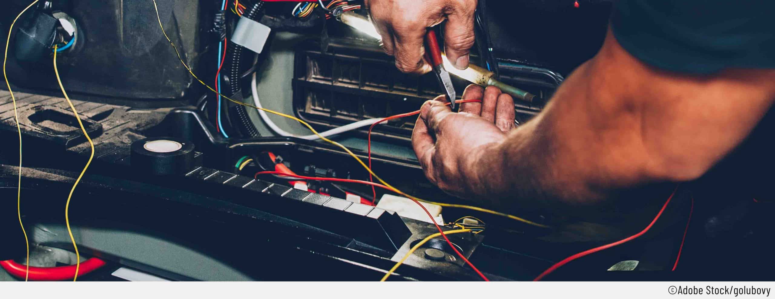 Ein Mechnaiker, repariert den Kabelbruch an einem Auto. Mit einer Kabelschere schneidet er das defekte Kabel, um eine Kabelbaum-Reparatur durchführne zu können.